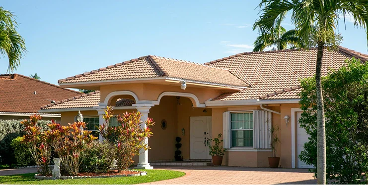 A welcoming single-story home with a tiled roof, surrounded by lush greenery and colorful plants.