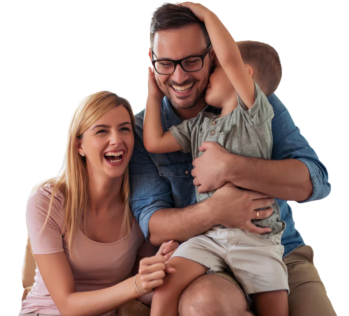 A happy family sits close together on a couch, sharing a warm embrace, with a young child resting comfortably on a parent's lap.