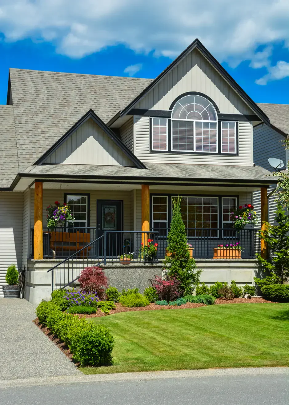 A charming two-story home with a gabled roof, surrounded by colorful flowers and manicured lawn under a clear blue sky.